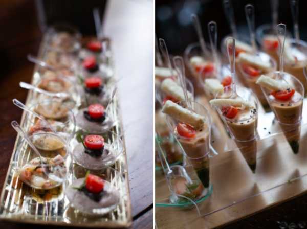 Close-up detail shot of cocktail hour canapés and amuse-bouche appetizers displayed in small clear plastic tasting cups and mini spoons, arranged in rows on clear acrylic serving trays. The left panel shows a line of shot-glass-style cups containing what appears to be a seafood or charcuterie preparation, each garnished with a cherry tomato half and a dark olive or berry, with a small clear spoon. The right panel shows a similar arrangement of mini cups filled with a creamy or mousse-based preparation, garnished with cherry tomato halves, black sesame seeds, and what appear to be small spring rolls or breadsticks. The presentation style is modern and minimalist, consistent with French cocktail hour catering service.