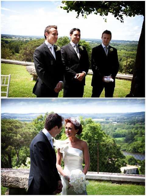 A composite of two outdoor ceremony images taken at an elevated terrace or balcony with sweeping countryside and river valley views. In the top image, three men in dark navy/black suits with light grey ties and white buttonhole flowers stand together — likely the groom and two groomsmen — one holding what appears to be a ring pillow. In the bottom image, the groom in a dark suit faces the bride, who wears a one-shoulder ivory structured gown and carries a bouquet of white peonies or orchids, with a decorative fascinator in her hair. Both images are wide/medium portrait shots taken in bright midday sunlight, with the landscape panorama serving as a natural backdrop. The styling is classic and formal.