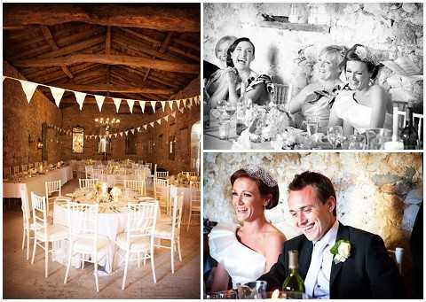 A collage of three wedding reception images from what appears to be a French stone barn venue. The left image shows a wide shot of the reception room setup with round tables dressed in white linens, white chiavari chairs, cream and gold centerpieces, cream bunting strung across the exposed wooden beam ceiling, and warm chandelier lighting against rustic stone walls. The top right image is a black-and-white close-up of three women — likely bridesmaids or guests — laughing at a long reception table, with glassware and table settings visible; the image has strong contrast with bright highlights and mid-range shadows. The bottom right image shows the bride and groom seated together at the reception, both smiling and laughing; the bride wears a white dress and a crystal or pearl tiara, while the groom wears a dark suit with a white boutonniere, with a wine bottle and table settings visible in the foreground against the stone wall background. Potential venue feature image.