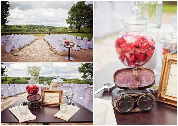 A collage of three outdoor wedding ceremony and decor detail shots with a vintage steampunk-inspired styling theme. The top-left wide shot shows rows of white chair-covered seats arranged along a petal-lined aisle in an open-air setting with rolling countryside views in the background; a small bistro table with a floral arrangement marks the ceremony space. The bottom-left detail shot shows a dark wooden display table set with glass apothecary jars filled with red candies and clear sweets, a gold-framed sign, vintage goggles, and small printed cards or programs, with baby's breath arrangements and more candy jars visible behind. The right close-up detail shot focuses on a pair of antique brown leather aviator-style goggles resting in front of a glass jar filled with red candies and a gold ornate picture frame, reinforcing the vintage or steampunk decor concept.
