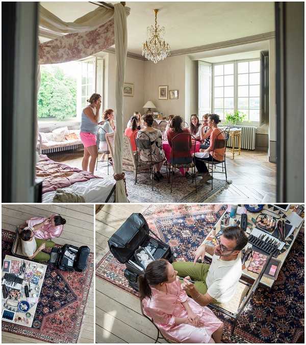 A three-panel composite image documenting the bridal getting-ready process inside what appears to be a chateau. The top image shows a wide shot of a large, light-filled room with a crystal chandelier, tall French windows, and parquet flooring, where approximately six to seven women are seated around a table having hair and makeup done, while two others stand near a four-poster bed draped in toile fabric in the foreground. The bottom-left panel is an overhead shot showing a woman in a pink satin robe seated near an open makeup kit with a large array of professional cosmetics and tools spread across a patterned rug. The bottom-right panel shows a male makeup artist in a white shirt and olive trousers applying makeup to a seated woman in a pink satin robe, with a mirrored makeup station and extensive brush collection visible, photographed from above.