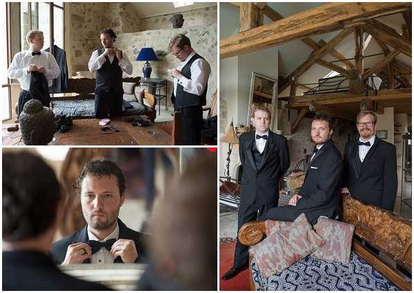 A collage of three getting-ready images featuring the groom and groomsmen dressed in classic black tuxedos with black bow ties and white dress shirts. Top left shows three men in a rustic stone-walled interior room helping each other adjust their attire, with a blue lamp and wooden furniture visible. Bottom left is a close-up portrait of the groom adjusting his bow tie in a mirror, captured from behind his shoulder. The right panel shows two men — likely the groom and a groomsman — posing together inside a barn-style room with exposed wooden ceiling beams, a rustic wooden sofa with patterned cushions, and a red-tiled floor, suggesting a French chateau or farmhouse venue. The overall styling is classic and formal.