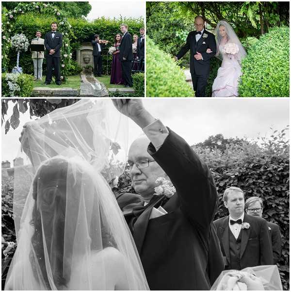 A collage of three images from an outdoor garden wedding ceremony. Top left shows the groom in a black tuxedo standing at the altar beneath a floral arch decorated with white and pale pink blooms, with a violinist performing and bridesmaids in burgundy dresses visible in the background. Top right shows the bride being walked down the garden path by an older gentleman, likely her father; she wears a pale blush pink ballgown with a long veil and carries a blush and white bouquet, with lush green hedging lining the walkway. The bottom image is black and white and shows a close-up mid-shot of the father lifting the bride's cathedral-length veil, with the groom visible in the background wearing a black tuxedo and bow tie and a second man in glasses also present; the image has soft contrast and captures the veil-lifting moment at the altar.