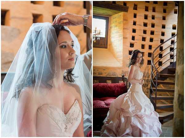 A diptych of two bridal portraits taken indoors in a rustic stone venue with warm-toned walls. The left image is a close-up portrait of the bride having her veil adjusted, wearing a strapless blush/champagne ballgown with beaded bodice detailing and a pendant necklace, with a sheer veil draped over her dark curled hair. The right image is a full-length portrait of the same bride standing beside a wrought-iron spiral staircase, her blush pick-up ballgown with a layered skirt fully visible, posed in front of a decorative square-pattern stone or wooden screen wall with a red upholstered sofa visible in the background. Both shots highlight the bride's blush gown and the rustic interior architecture of what appears to be a chateau or stone manor.