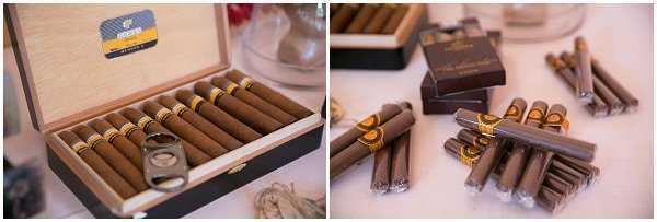 Close-up detail shots of a cigar station set up at a wedding reception, presented as a diptych. The left image shows an open wooden cigar box filled with branded cigars featuring gold and brown bands, with a cigar cutter resting on top. The right image shows cigars bundled and stacked on a white linen-covered table alongside dark brown branded matchboxes or cigar boxes. The styling suggests a curated guest amenity or cigar bar station, likely part of a cocktail hour or reception setup.