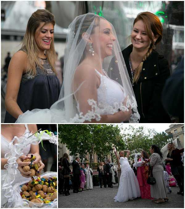 A three-image collage capturing an outdoor wedding celebration, likely a traditional or cultural ceremony taking place in a town square or public plaza. The top image is a close-up portrait of a bride in a white lace strapless gown with a lace-edged veil, laughing alongside two female guests — one in a dark navy embellished dress and one in a black jacket. The bottom-left image is a detail close-up of a decorative tray or basket holding walnuts, wrapped chocolates or sweets in colorful foil, and white ribbon decorations, likely traditional wedding favors or confetti offerings. The bottom-right wide shot shows the bride in her white ball gown dress celebrating outdoors in a tree-lined plaza surrounded by a crowd of approximately 15–20 guests dressed in a mix of formal and colorful traditional attire, with the bride raising her arms in a celebratory gesture.