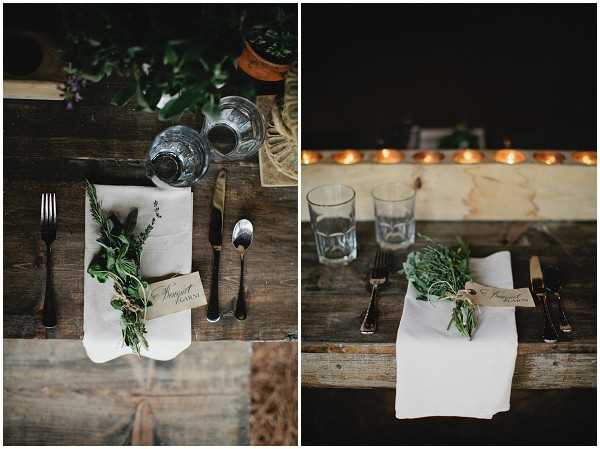 Close-up detail shots of rustic wedding table settings shown as a diptych. Each place setting features a white linen napkin topped with a small fresh herb bundle — including rosemary and thyme — tied with twine and accompanied by a small calligraphy place card reading 'Bouquet Garni.' The flatware is dark/black-handled, and clear glassware is set alongside. The table surface is raw, unfinished dark wood. The right image shows a row of lit tea light candles along the back edge of the table, casting warm amber light against a dark background. The styling is rustic and organic, with an earthy, herb-garden-inspired decor palette. Both shots are close-up detail/flat-lay style compositions taken from slightly above.