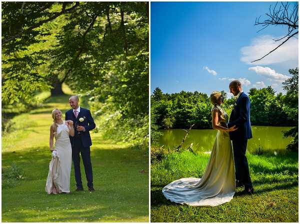 A diptych of two outdoor couple portrait shots taken in a parkland setting featuring a pond or small lake. In both images, the bride wears a floor-length ivory satin gown with a halter neckline and a long train, while the groom wears a navy suit with a white boutonniere. In the left image, the couple stands on a grassy path beneath large leafy trees, smiling and facing the camera in a relaxed mid-shot pose. In the right image, the couple faces each other in a close romantic pose on the bank of a reflective pond, shot from a low angle with vivid blue sky above, emphasizing the gown's long train spread on the grass. Both shots are full-length portraits with saturated, bright natural lighting typical of a sunny summer day.