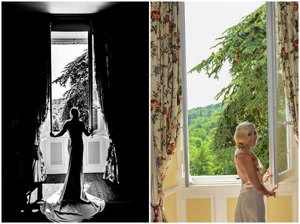 A diptych of two getting-ready portraits, both taken inside what appears to be a chateau room with tall French doors. The left image is black-and-white, showing a bride in silhouette standing in an open doorway with her long cathedral-length veil and fitted gown trailing behind her; the high contrast between the bright exterior light and the dark interior creates a strong graphic composition. The right image is a color portrait of the same bride, a blonde woman in a silver-grey satin slip-style gown, glancing back over her shoulder while standing at an open window framed by cream floral-print curtains with red and green botanical motifs; the room features yellow-painted walls. Both shots are medium full-length portraits that emphasize the interior setting and the bride's dress, with the window and door openings used as compositional framing devices.