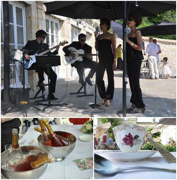 A three-image collage showing cocktail hour entertainment and reception details at an outdoor French venue. The top image shows a live band performing under large black umbrellas on a stone courtyard in front of a limestone building: two male musicians in black outfits playing electric guitars and two female vocalists in black strapless jumpsuits singing into a vintage-style microphone, with wedding guests visible in the background. The bottom-left detail shot shows a silver champagne ice bucket holding two bottles of rosé champagne on a white linen-covered table, with glassware and small plates visible. The bottom-right close-up shows a vintage floral-patterned teacup and saucer in white with a pink rose motif, accompanied by a spoon and a small tag, styled in a classic or vintage theme. Potential venue feature image.