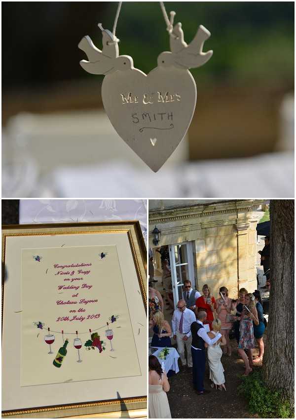 A three-image collage of wedding details and guests at Chateau Lagorce, dated 20th July 2013. The top image is a close-up detail shot of a white painted wooden hanging heart ornament featuring two doves and the text 'Mr & Mrs Smith', suspended against a softly blurred outdoor background. The bottom-left image shows a framed congratulatory print in a gold frame, illustrated with wine bottles, glasses, and grape motifs in red and green, reading 'Congratulations Nicole & Greg on your Wedding Day at Chateau Lagorce on the 20th July 2013', reflecting a wine-themed decor element. The bottom-right image is a wide shot of approximately 15 guests mingling outdoors during a cocktail hour against the stone facade of the chateau, with the bride in an ivory gown visible among the group; guests are dressed in smart-casual summer attire in various colors including red, blue, and floral prints.