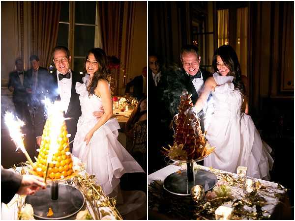 A two-panel image capturing a cake cutting moment at an indoor evening reception, set in what appears to be a formal chateau or grand salon with warm amber lighting. The bride wears a white strapless ballgown with a ruffled skirt, and the groom is dressed in a black tuxedo with bow tie. In the left panel, the couple stands smiling beside a traditional French croquembouche — a tower of choux puffs — decorated with gold accents and lit sparklers placed around its base on a silver tray. In the right panel, the bride is actively cutting into the croquembouche, now smoking from the extinguished sparklers, with caramelized profiteroles visible in the structure. The table displays gold leaf decorative elements and small votive candles, with other formally dressed guests visible in the dimly lit background. Both panels are close-to-medium portrait shots with warm, low-light reception ambiance.