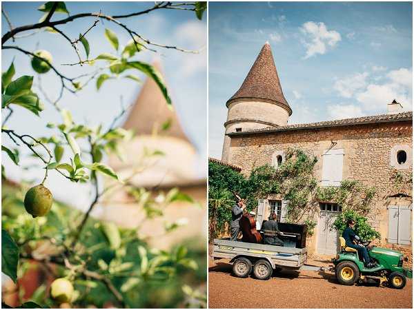 A diptych image showing two scenes at a French countryside chateau venue. The left panel is a close-up detail shot of a fruit tree branch with small green fruits, with the chateau's conical tower visible softly out of focus in the background. The right panel is a wide shot showing the exterior of a stone chateau with a distinctive round tower and terracotta-tiled conical roof, where three musicians — one playing double bass, one playing violin, and one seated at an upright piano — are being transported on a flatbed trailer pulled by a green John Deere ride-on tractor across the gravel courtyard, likely arriving to perform at the wedding. The candid, humorous scene adds an informal character to the venue arrival. Potential venue feature image.