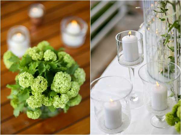 Close-up detail shots of wedding reception decor displayed as a side-by-side diptych. The left panel shows an overhead view of a compact floral arrangement of lime green viburnum (snowball flowers) with lush green foliage in a glass vase, placed on a wooden surface alongside small glass tea light holders with lit candles. The right panel shows white pillar candles in clear glass hurricane holders and stemmed glass candleholders arranged on a white linen surface, with a tall glass cylinder vase containing green trailing foliage and warm fairy lights visible in the background, along with a partial lime green viburnum arrangement at the edge. The overall decor palette is crisp white and lime green with a clean, modern styling approach.