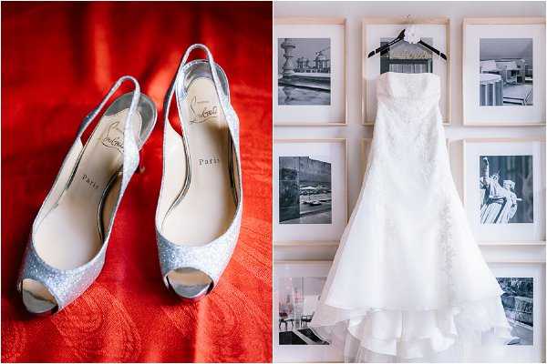 A split detail shot featuring two bridal accessories. On the left, a pair of silver glitter Christian Louboutin peep-toe slingback heels are displayed against a vivid red fabric background, with the brand name and 'Paris' visible on the insoles. On the right, an ivory strapless fit-and-flare wedding dress with lace detailing hangs from a hanger adorned with a small white floral accent, displayed against a gallery wall of black-and-white framed photographs in light wood frames. The composition is a close-up detail flat lay on the left paired with a portrait-style hanging shot on the right, reflecting a classic, polished bridal styling aesthetic.