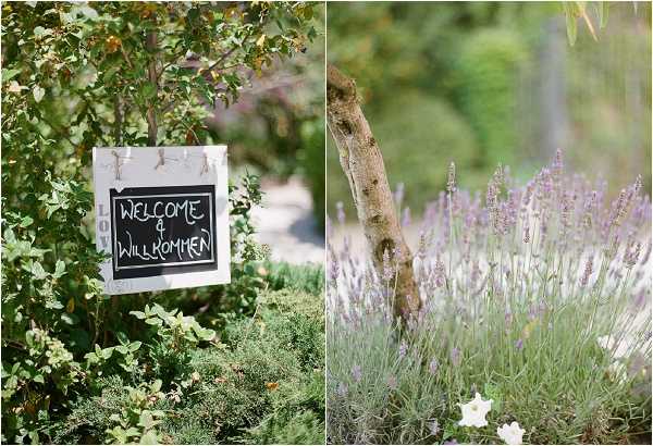 A two-panel detail shot taken outdoors in a garden setting. The left panel shows a small chalkboard welcome sign reading 'Welcome & Willkommen' hung with twine from a leafy shrub, indicating a bilingual (English and German) wedding. The right panel shows a close-up of blooming lavender plants in soft purple alongside a small tree trunk, with a white flower visible at the lower edge of the frame. Both shots have a soft, light-filled quality consistent with outdoor natural light photography.