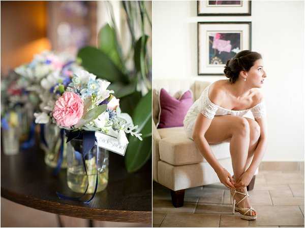 A two-image composite showing getting-ready details. On the left, a close-up of bridesmaid bouquets arranged in glass mason jars tied with navy blue ribbon, featuring blush pink garden roses, pale blue delphinium, dusty miller, and small purple accent flowers, with small tags labeled 'bridesmaid' attached; multiple bouquets are visible in a row on a dark wooden surface. On the right, a portrait of the bride seated on a cream upholstered chair in an indoor room, wearing a short white lace dress and fastening strappy gold heeled sandals; her dark hair is styled in an updo and she wears drop earrings, with purple accent pillows and framed artwork visible on the wall behind her.