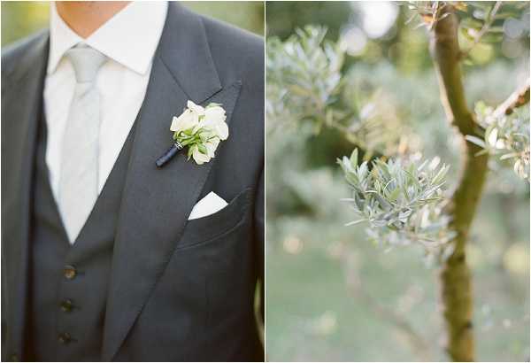 A diptych of two close-up detail shots taken outdoors. The left image shows the torso of a groom wearing a charcoal grey three-piece suit with a light grey tie, a white pocket square, and a boutonniere featuring small ivory flowers with green foliage wrapped in dark ribbon. The right image is a shallow-focus close-up of an olive tree branch with silvery-green leaves, softly blurred in the background, suggesting a southern French or Mediterranean outdoor setting.