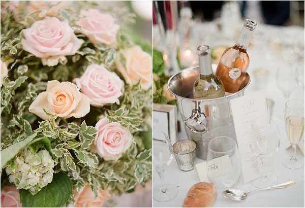 A split image showing two reception detail close-ups. The left panel features a floral centerpiece arrangement with blush pink and peach garden roses, white hydrangeas, and variegated green-and-white foliage. The right panel shows a silver wine/champagne bucket holding two bottles — one white wine and one rosé — placed on a white-linen reception table set with champagne flutes, a small mercury glass votive, printed menus or place cards, a bread roll, and silverware, with candles softly lit in the background. The overall decor palette is blush, peach, silver, and white, suggesting a classic and romantic styling approach.