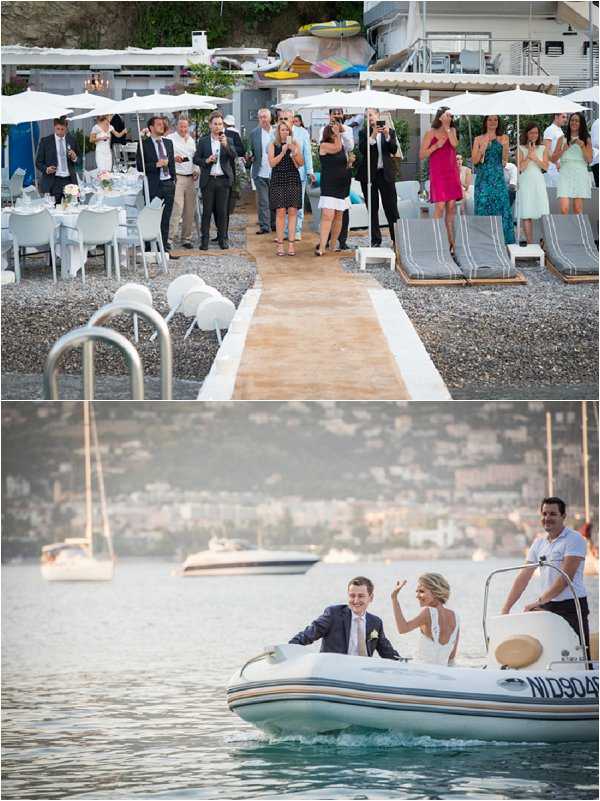 A two-image composite showing a beach wedding reception and couple arrival by boat. In the top image, approximately 20 guests stand and applaud along a wooden boardwalk aisle on a pebble beach, with white round tables set for dining on the left side and grey lounge chairs with white parasols on the right; guests are dressed in smart-casual attire including a hot pink dress, teal dress, and light green dress among others. In the bottom image, the bride and groom arrive by white rigid inflatable boat on the water, with a coastal town and sailboats visible in the background; the groom wears a navy suit with a light pink tie and boutonniere, while the bride wears a sleeveless open-back white gown and waves to the guests on shore. The overall style is a relaxed coastal beach reception with a casual-chic aesthetic. Wide shots are used for both frames.