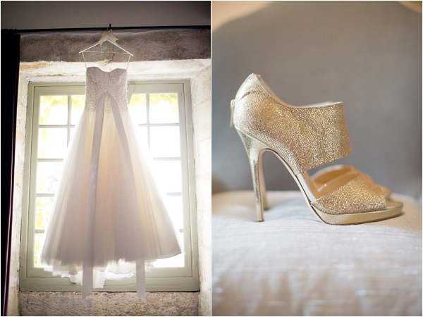 A two-image flat lay and detail collage showing bridal accessories during a getting-ready phase. On the left, a strapless sweetheart-neckline wedding dress with a heavily crystal-embellished fitted bodice and a full, layered tulle skirt in ivory hangs from a clear hanger against a multi-paned stone-framed window, with natural backlight illuminating the skirt. On the right, a close-up detail shot of a single gold crystal-encrusted platform stiletto heel with an open toe and wide ankle strap, resting on a white surface, likely a bed. The overall styling suggests a classic-glam aesthetic with a focus on beading and sparkle details.