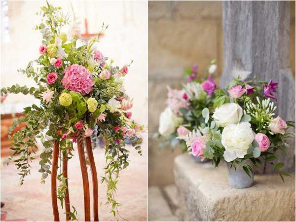Close-up detail shots of wedding ceremony floral arrangements in a two-image composite. The left image shows a tall pedestal arrangement mounted on wooden copper-toned stands inside what appears to be a church or chapel, featuring pink hydrangeas, chartreuse carnations or viburnum, hot pink spray roses, white blooms, and cascading eucalyptus and trailing greenery in a lush, garden-style arrangement. The right image shows a compact arrangement in a small grey zinc or concrete pot placed on a stone ledge, containing white peonies, blush and hot pink roses, purple bell-shaped flowers, white veronica or freesia spikes, and eucalyptus foliage. Both arrangements share a pink, white, and green color palette with a romantic garden-style aesthetic.