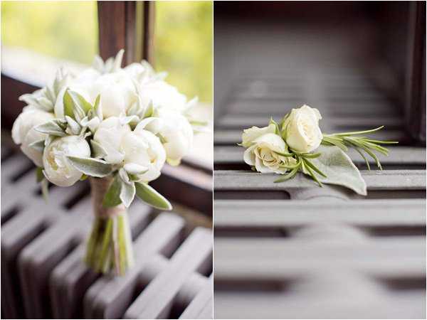 A split detail shot showing two floral arrangements resting on what appears to be a dark wooden slatted surface, likely a bench or chair. On the left, a bridal bouquet composed of white peonies and ivory ranunculus with silver-green lamb's ear foliage, wrapped with natural twine at the stem. On the right, a matching boutonniere featuring a single cream spray rose with rosemary sprigs and a lamb's ear leaf. Both arrangements follow a minimal, classic palette of white and soft green, consistent with a clean, understated floral design scheme. Close-up detail shots with shallow depth of field.