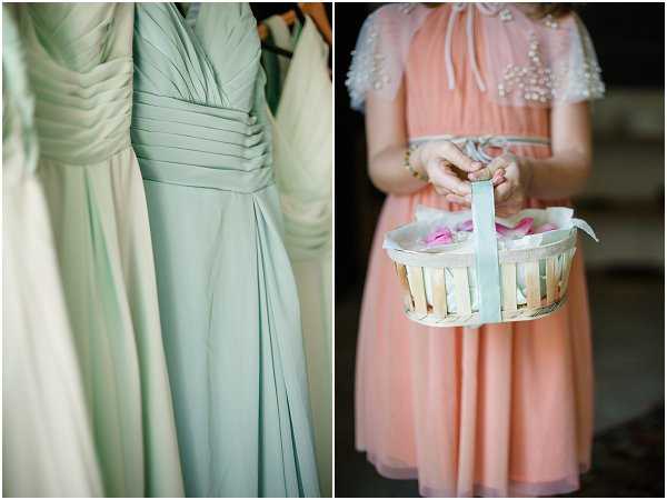 A two-image detail composition showing wedding party preparations. On the left, three mint green chiffon bridesmaid dresses hang on a rack, featuring ruched bodices and floor-length skirts in a classic silhouette. On the right, a young flower girl wearing a coral/peach short dress with pearl-embellished cap sleeves holds a small white wooden slat basket trimmed with a mint green ribbon, containing pink rose petals. The color palette coordinates the mint green accents across both images, suggesting a deliberate mint and coral/peach styling theme. Both shots are close-up detail portraits with soft, diffused lighting.