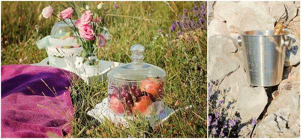 A styled detail shot presented as a diptych. The left image shows an outdoor picnic-style vignette set in a grassy area, featuring a glass cloche covering fresh strawberries and cherries placed on a white doily, alongside a small vase with pink ranunculus and white flowers, a mint green decorative item, and a purple woven textile draped nearby — suggesting a romantic outdoor picnic setup with a pastel and jewel-tone palette. The right image is a close-up detail of a polished silver champagne bucket or ice pail resting against a stone wall, with lavender visible in the foreground. The overall styling has a rustic-romantic, French countryside aesthetic.