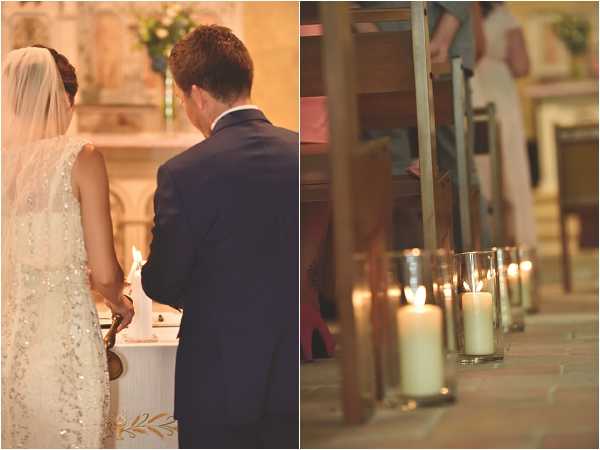 A diptych of two ceremony images taken inside a chapel or church. On the left, the bride and groom stand together at the altar with their backs to the camera, holding hands; the bride wears a heavily embellished, beaded ivory gown with a long veil, and the groom wears a navy suit. On the right, a close-up detail shot shows a row of pillar candles in clear glass hurricane holders lining the stone-floored church aisle, with wooden pews and the bridal party softly out of focus in the background. The warm candlelight and stone interior suggest a classic, candlelit ceremony style.
