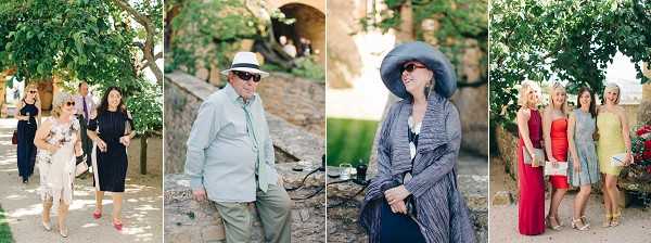 A collage of four candid guest photographs taken outdoors at what appears to be a French château or stone-walled venue during a cocktail hour or reception. The first panel shows two women walking together, one in a floral dress and one in a black dress. The second panel features a man in khaki trousers, a light blue shirt, and a white panama hat leaning against a stone wall. The third panel shows a woman seated outdoors wearing a wide-brimmed grey hat, grey wrap cardigan, and printed dress. The fourth panel features a group of four women posing together, dressed in a red halter gown, yellow dress, grey patterned dress, and a fourth in a light-colored outfit. All images are wide and medium shots with a bright, natural light aesthetic, suggesting a warm-weather outdoor celebration with guests dressed in smart-casual to formal attire.