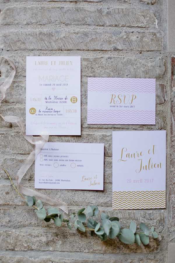A flat lay detail shot of a four-piece French wedding stationery suite for Laure et Julien, dated 29 avril 2017, arranged on a pale stone or brick surface. The suite includes a main invitation card, an RSVP card, a response envelope, and a save-the-date or program card, all in a coordinated palette of blush pink, white, and gold. The design features gold script typography and a chevron pattern in both blush pink and gold across the cards. A sprig of eucalyptus and a length of ivory silk ribbon are styled alongside the stationery as decorative accents.