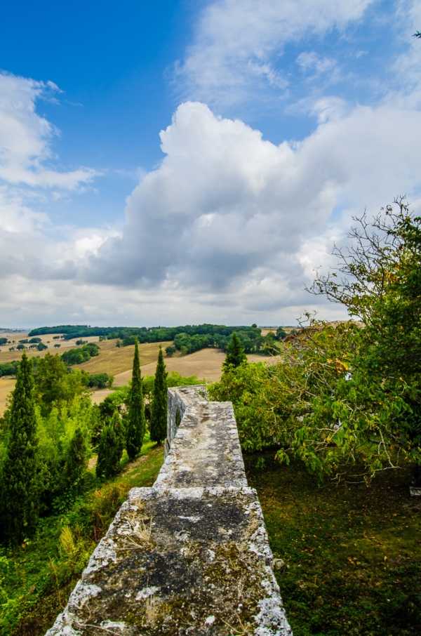 A wide-shot landscape view taken from atop a stone balustrade or parapet wall, looking out over rolling countryside with cypress trees and open fields in the distance. No people, wedding party, or ceremony elements are visible in this image. The shot appears to document the venue's elevated outdoor terrace or rampart and the surrounding rural landscape. Potential venue feature image.