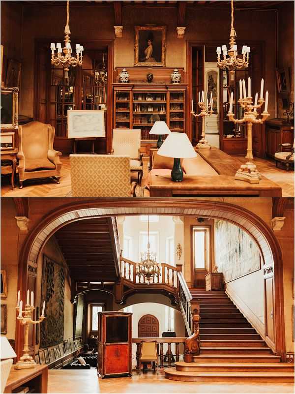 A two-panel interior shot of a French chateau venue with no wedding party present. The top panel shows a formal library or salon with parquet flooring, dark wood bookcases, antique wingback chairs, a large framed portrait painting above the central bookcase, two ornate gold candelabra chandeliers, and a table lamp with a cream shade. The bottom panel shows a grand entry hall featuring a wide arched doorway, a sweeping wooden staircase with carved balustrades, a brass chandelier, tapestries on the walls, candelabras on a side console, and antique furniture pieces including a decorative cabinet. Both rooms are warmly lit with amber tones and feature classic French chateau interior styling with wood paneling and period furnishings. Wide architectural shots showcasing the venue interiors. Potential venue feature image.