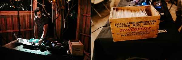 A side-by-side detail shot taken at a wedding reception in what appears to be a rustic barn venue. On the left, a male DJ wearing glasses and a dark short-sleeve shirt works at a DJ setup illuminated by warm ambient lighting, with wooden barn structure visible in the background. On the right, a close-up of a vintage wooden Winchester Small Arms Ammunition crate repurposed as a card or menu holder, filled with white paper inserts and placed on a black linen-covered table, serving as a rustic decorative element consistent with a country or barn-style wedding theme.