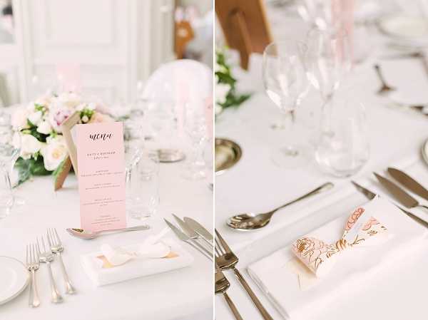 Close-up detail shots of wedding reception table settings in a bright, white interior venue. The left image shows a round table with a white linen, silver cutlery, crystal wine glasses, a blush pink printed menu card, a small white folded paper detail on a white square plate, and a low floral centerpiece featuring white and blush pink roses with greenery. The right image shows a close-up of a single place setting with a white linen napkin folded to hold a blush pink and gold floral-illustrated card, accompanied by silver cutlery and crystal glassware. The overall decor palette is white, blush pink, and gold with a classic, refined styling.