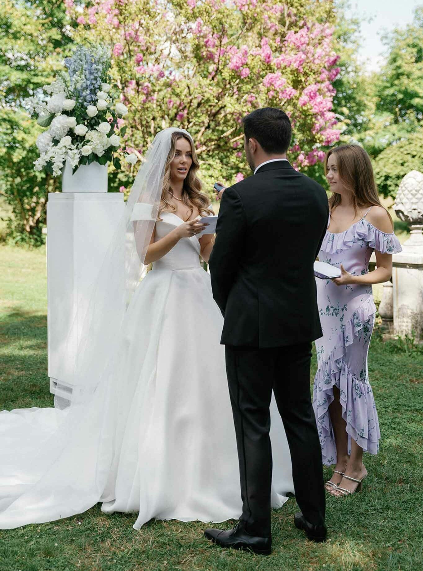 Bride and groom exchanging vows during outdoor garden ceremony with floral backdrop