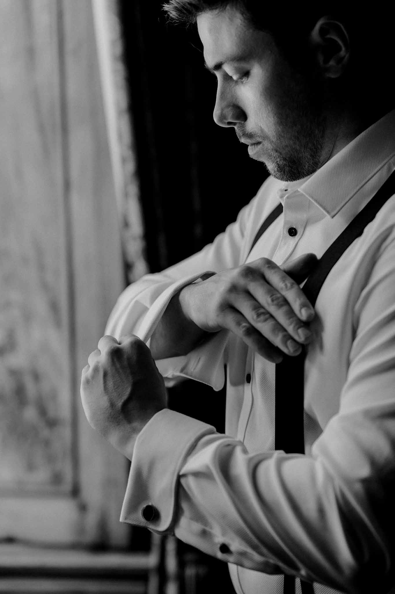 Groom fastening dress shirt during wedding preparation in black and white portrait