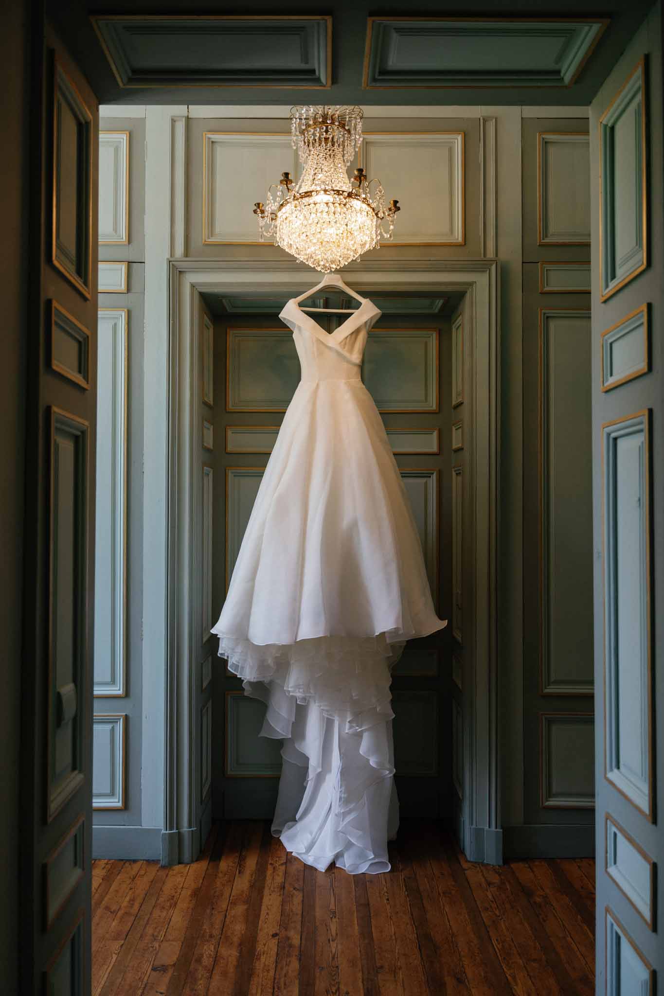 Ivory silk wedding gown with off-shoulder design displayed in classical interior with sage green paneled walls