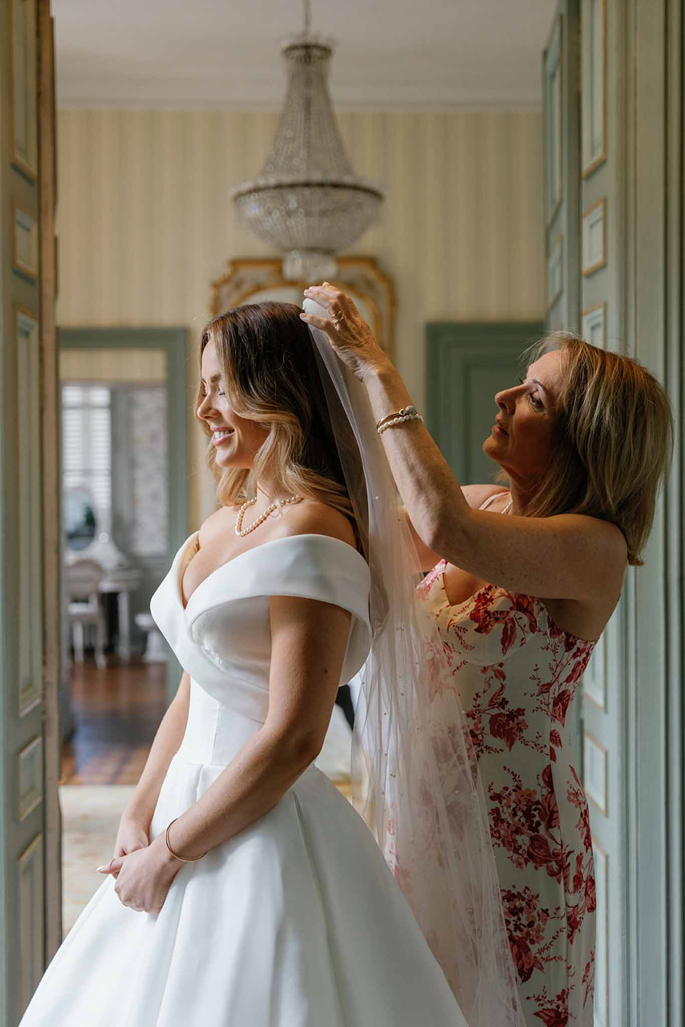 Bride having veil adjusted by bridesmaid in elegant hallway during wedding preparations