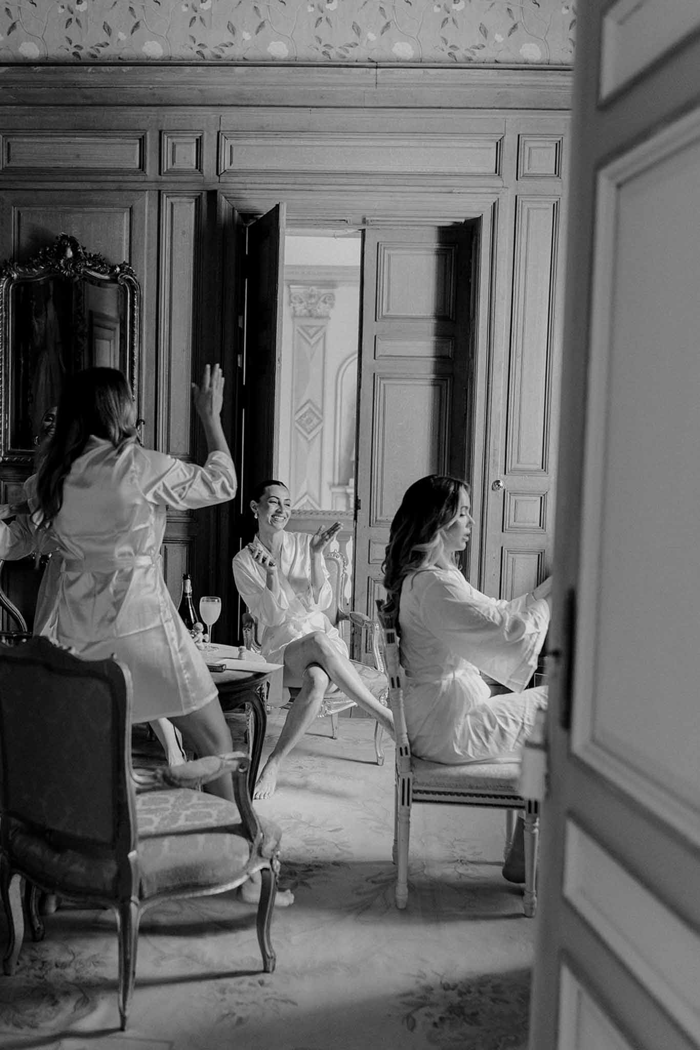 Three women in robes preparing for wedding in classic French château interior with paneled walls