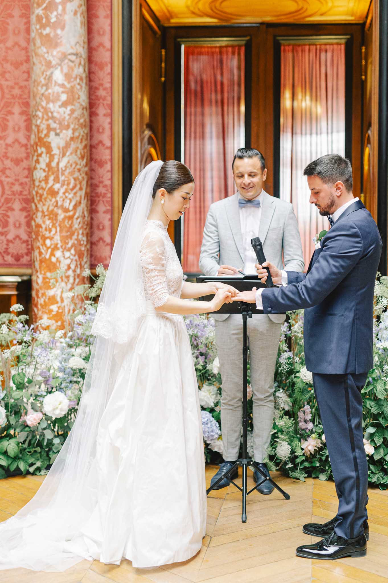 Ring exchange at indoor altar flanked by white peony pink and lavender hydrangea arrangements