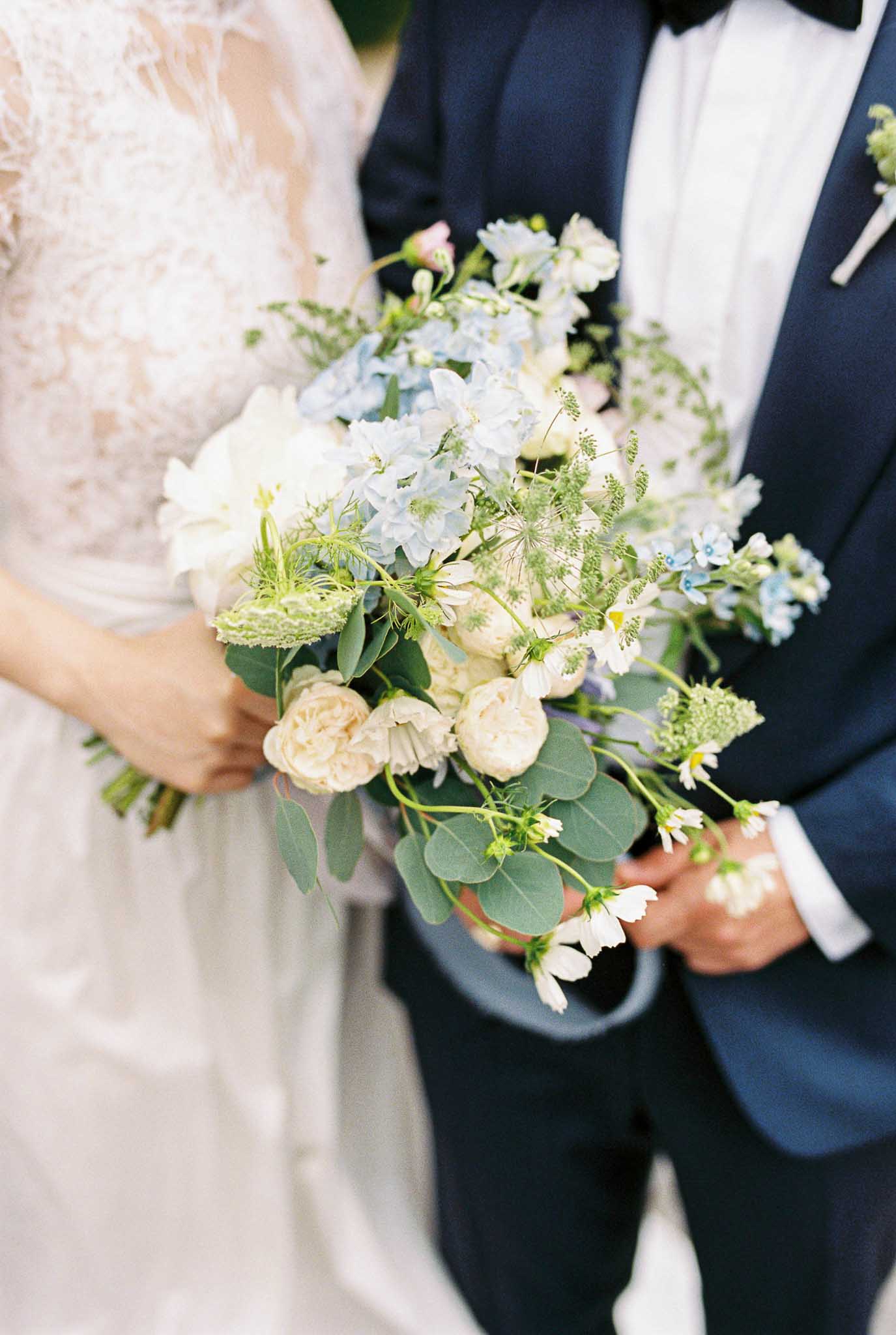 Close-up bridal bouquet of blue hydrangeas blush roses white queen anne's lace and eucalyptus with navy suit