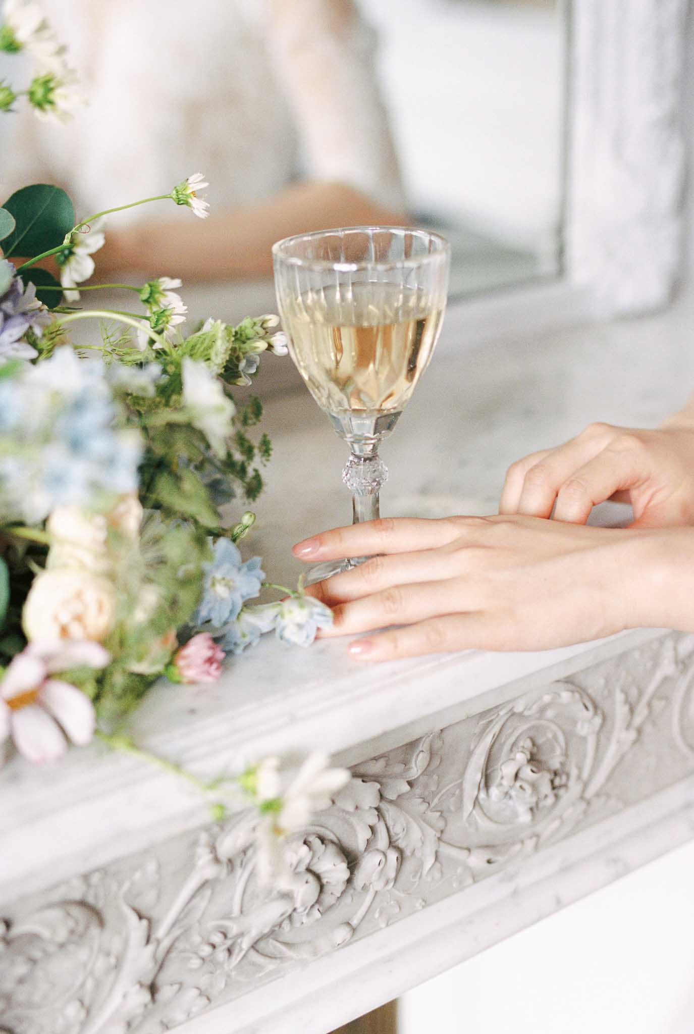 Bridal bouquet of peach roses, blue delphinium, and blush tulips on carved marble fireplace mantel