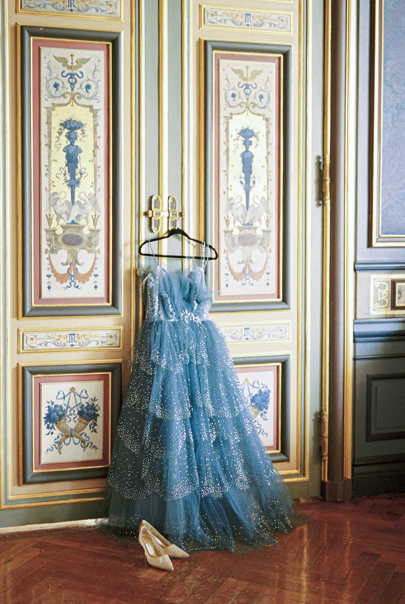 Blue tulle gown with silver embellishments hung in ornate boiserie room with gold-trimmed panels