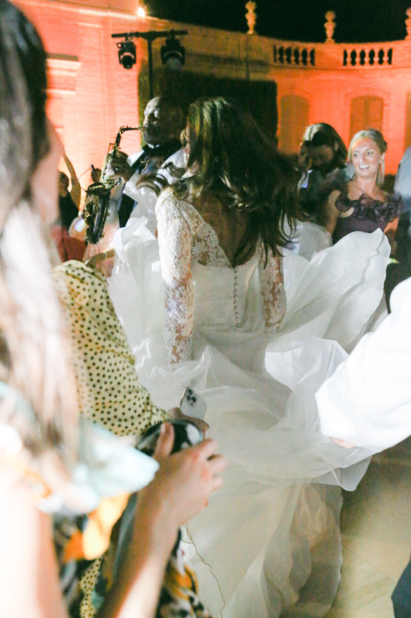 Bride dancing outdoors at night with swirling organza skirt saxophonist and uplighting on chateau