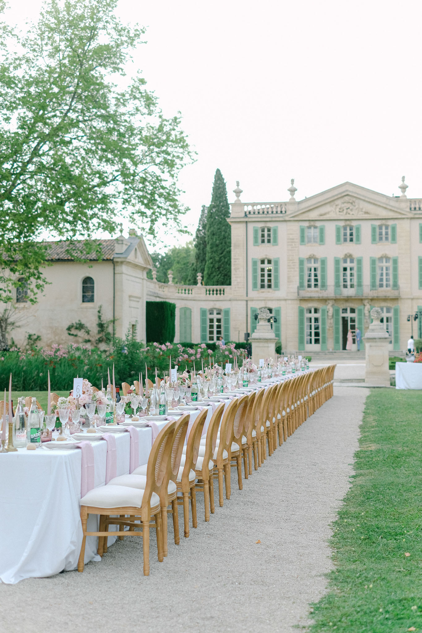 Long feasting table with blush runners and floral centerpieces on gravel path in front of French chateau