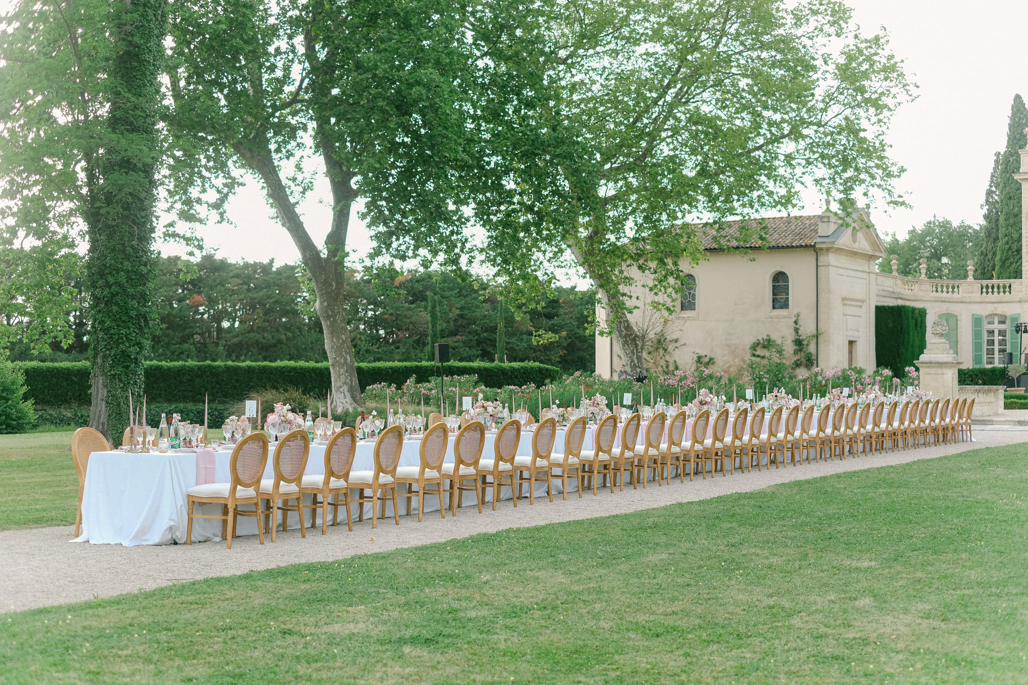 Long banquet table with gold Louis XVI chairs and blush floral arrangements set on chateau grounds