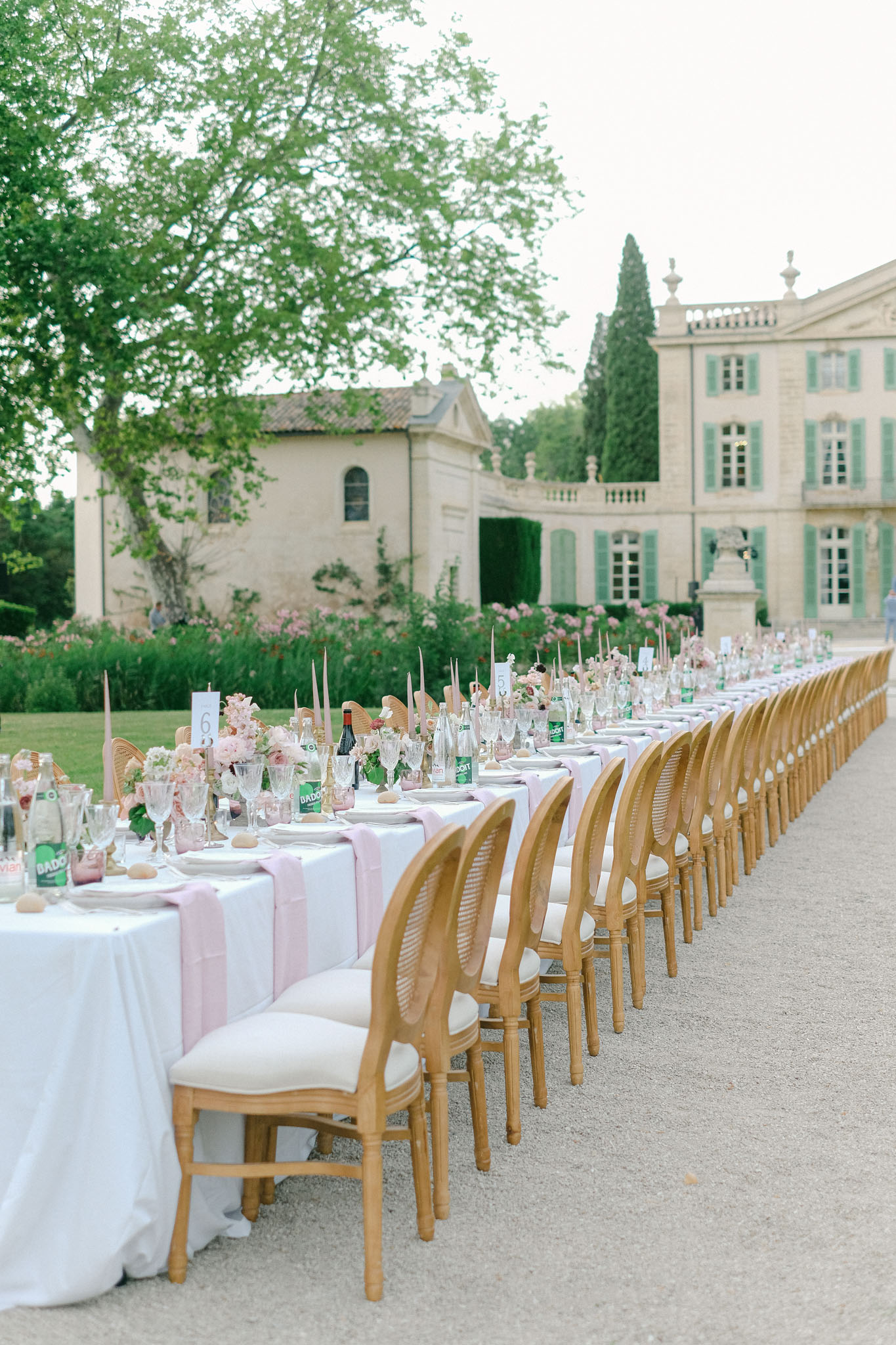Long banquet table with blush runners and pink florals on gravel courtyard in front of French chateau