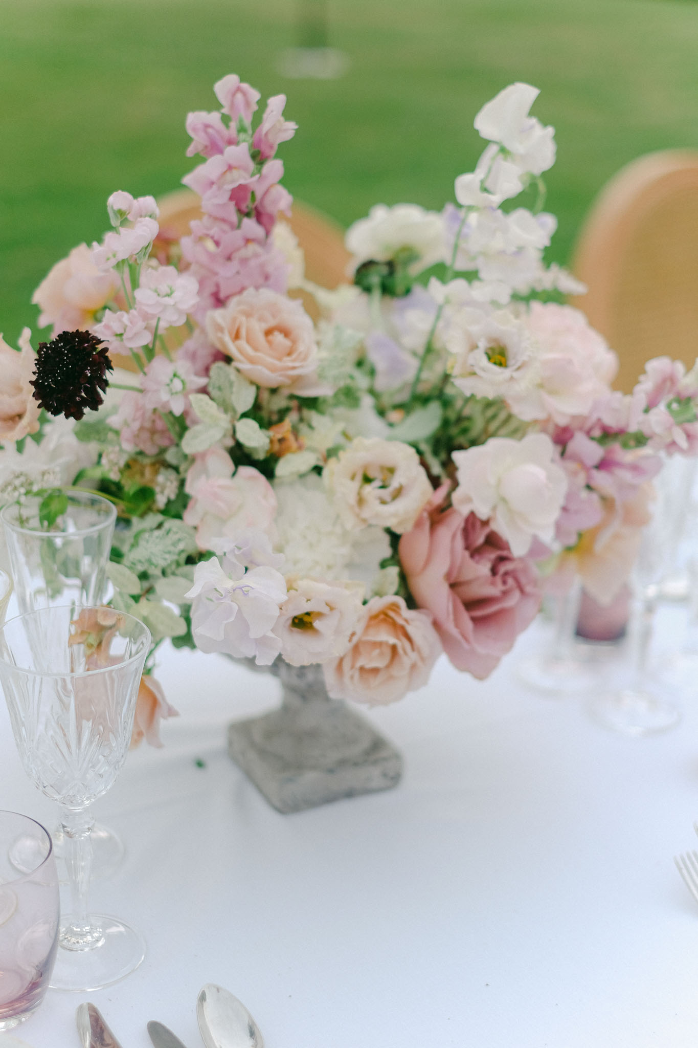 Reception table centerpiece in stone urn with blush roses, peach garden roses, and white sweet peas